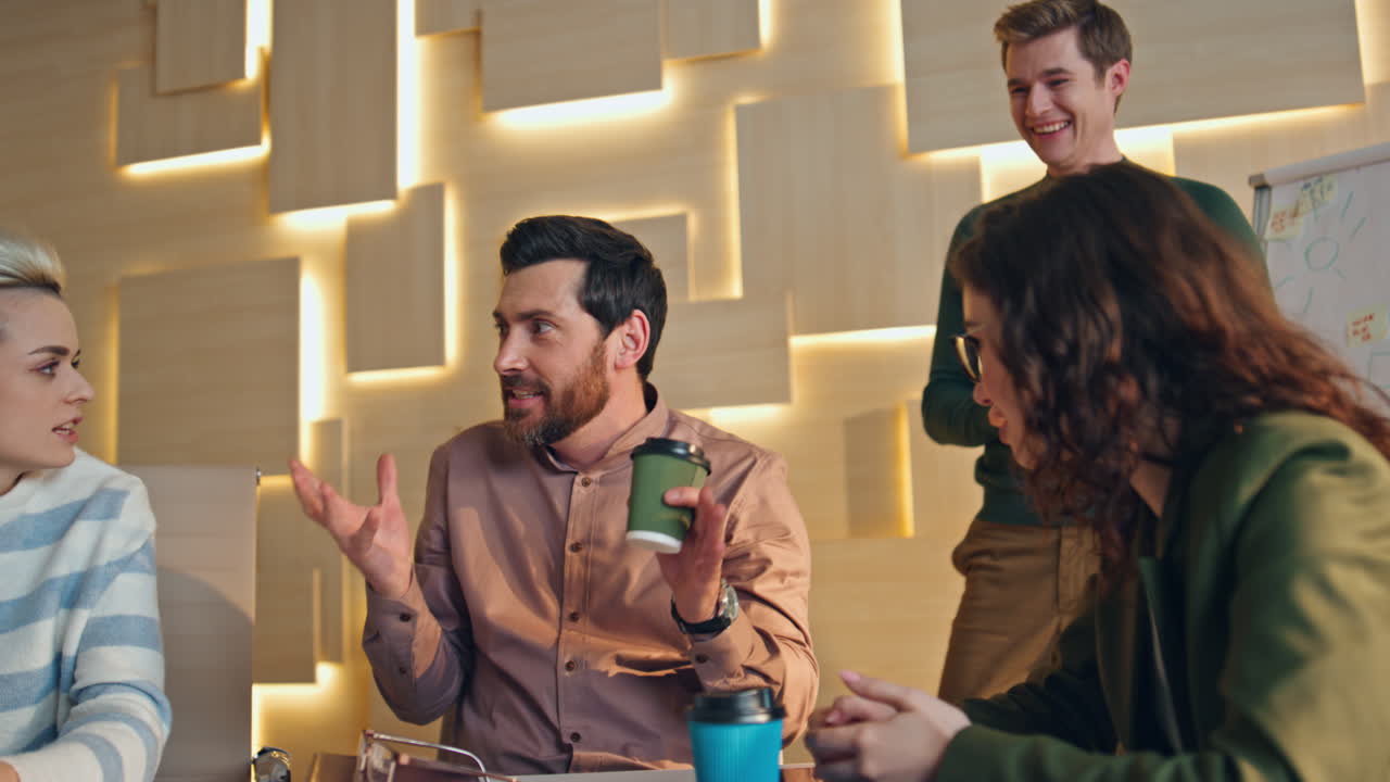 Gruppe smilende kolleger taler i kaffepause og sidder ved mødelokale skrivebord tæt på