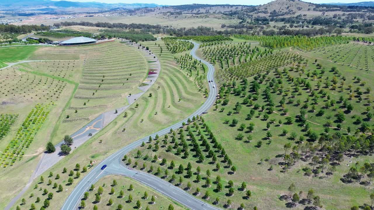Drone aerial landscape of cars driving down winding road surrounded by trees on hill in forest valley estate Botanical Gardens National Arboretum park Canberra ACT Australia travel tourism rural