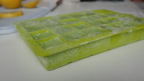 frozen lemonade cubes being popped out of the tray with a hand, close-up shot