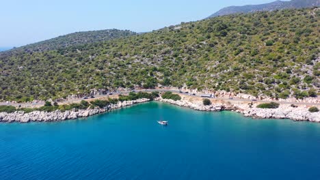 Wide-aerial-of-a-sailboat-anchored-in-the-tropical-blue-Mediterranean-Sea-near-Finike-Turkey-alongside-a-green-hill-and-coastal-highway-road