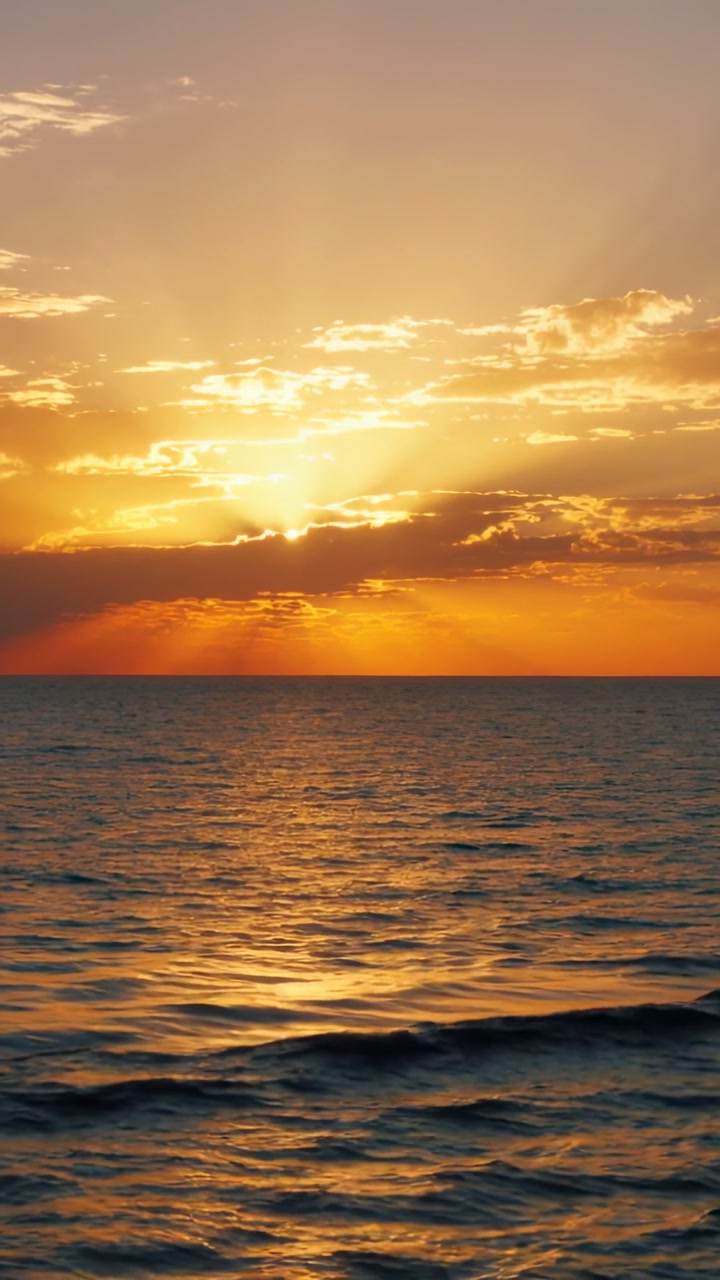 Glowing sun near horizon painting orange sky over open ocean at sea level, with cloud bank