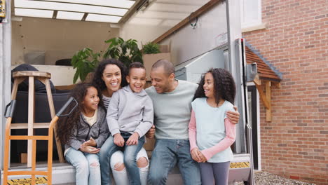 portrait of family sitting on tailgate of removal truck outside new home