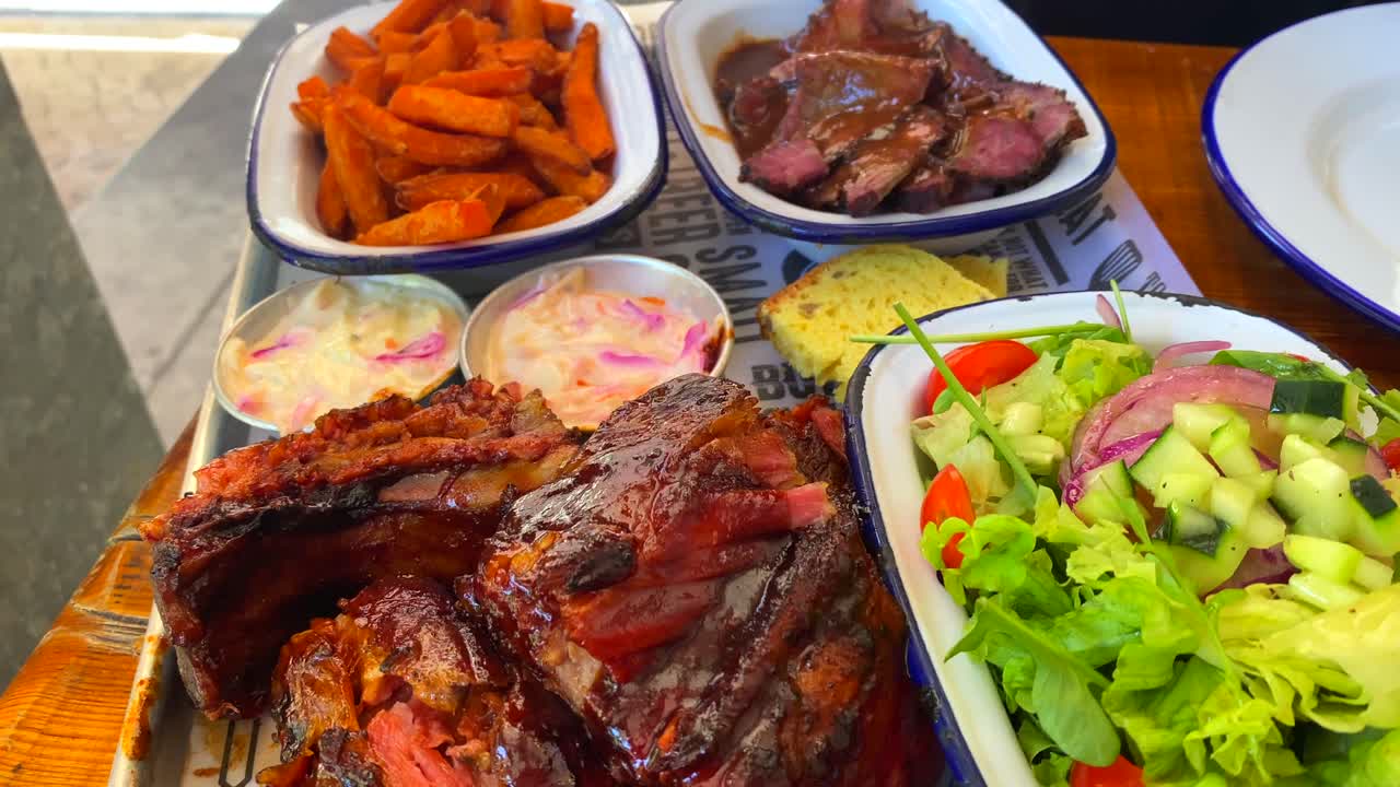 tiro dinámico de pechuga de ternera con ensalada, costillas de cerdo con batatas fritas, pan de maíz y ensalada de col, comida tradicional americana en un restaurante, 4k