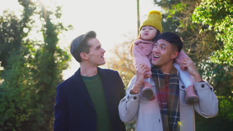 family with two dads on walk in winter countryside carrying daughter on shoulders