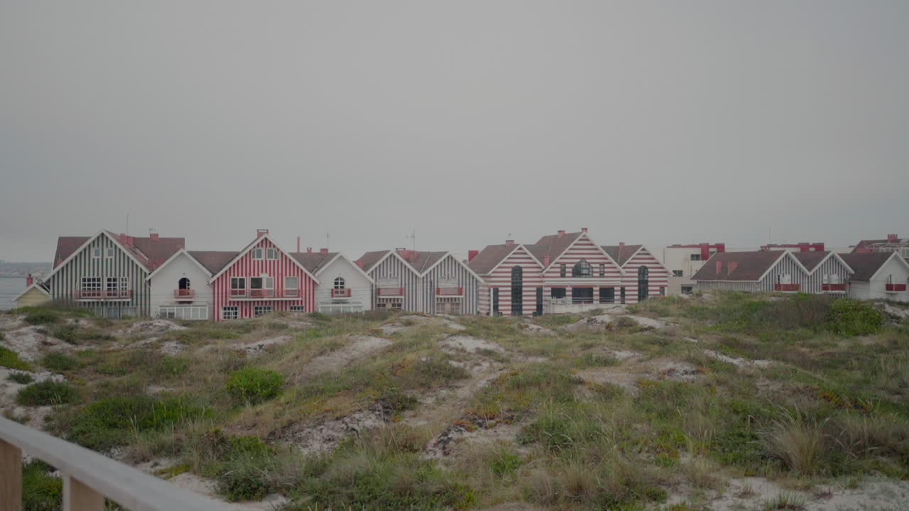 casas de colores rayados en praia da costa nova en aveiro, portugal, con dunas de arena en primer plano