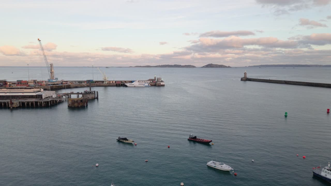 St Peter Port Limanı, Guernsey, alacakaranlıkta liman girişinden feribot rıhtımlarını ve iskeleleri, Herm, Jethou ve Sark manzarası eşliğinde bağlı tekneleri gösteren sakin bir gündeki drone görüntüleri