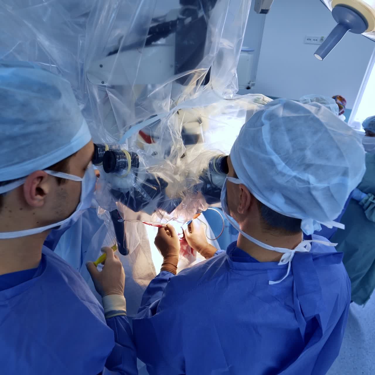 Approaching two neurosurgeons looking through the microscope at modern surgery room. High angle view. Medical staff at backdrop
