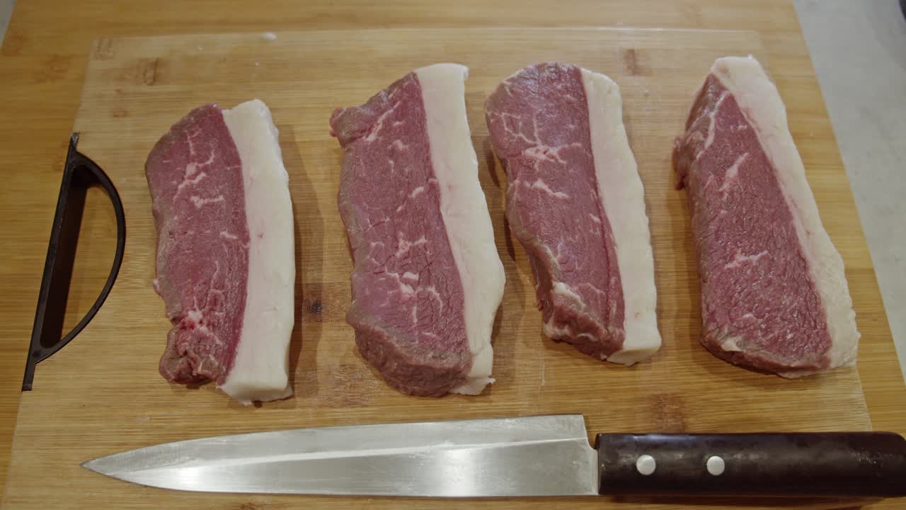 cuatro bistecs de carne y un cuchillo de cocina encima de una tabla cortada de madera