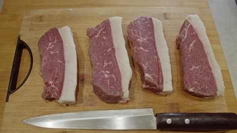 cuatro bistecs de carne y un cuchillo de cocina encima de una tabla cortada de madera