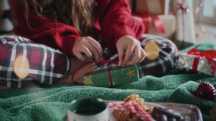 Woman making ribbon bow on wrapped Christmas gift at home