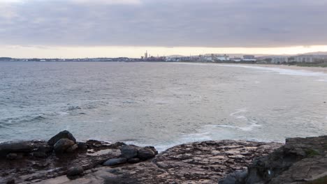 rocky shoreline with distant view of industrial landscape on cloudy day