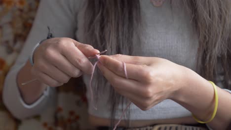 Woman-in-grey-ribbed-shirt-begins-to-use-hands-to-crochet-with-needles-and-yarn