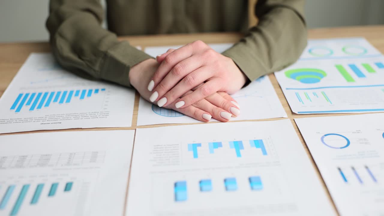Person's Hands Resting on Desk Among Business Charts and Graphs