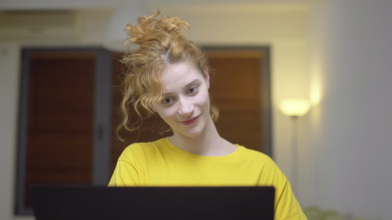 Cute girl sitting in living room infront of a laptop computer. Dancing happy with earphones. Portrait of a student taking online course. Home education concept.