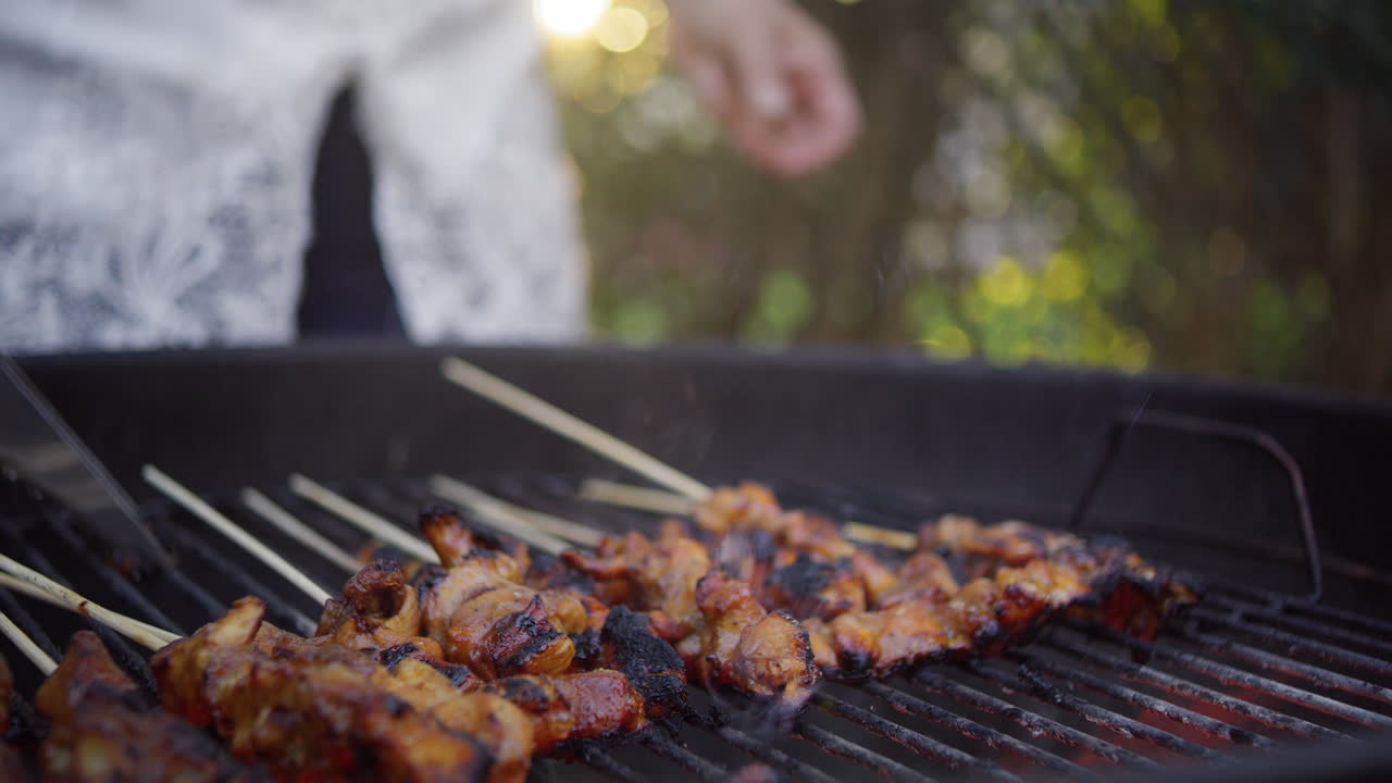 mujer indonesia asa satay de pollo sobre carbón en su patio trasero