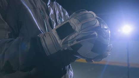 close-up of gloved hands rubbing a worn soccer ball during an evening training session on an urban field, bright lights in the background