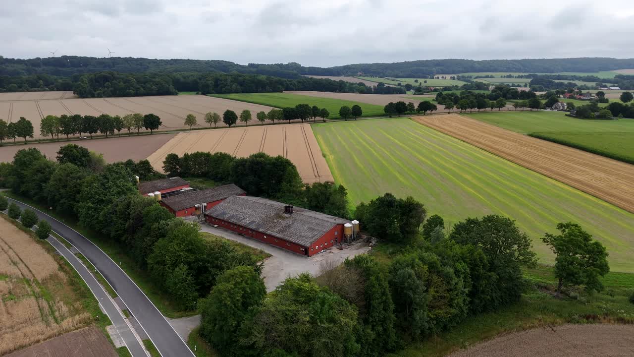 Red Barn farmstead in Minnesota state during sunny summer day. Wheat fields and car on rural intersection road. Green growing hills of United States. Aerial wide shot