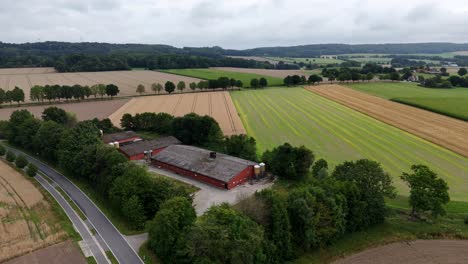 red barn farmstead in minnesota state during sunny summer day. wheat fields and car on rural intersection road. green growing hills of united states. aerial wide shot