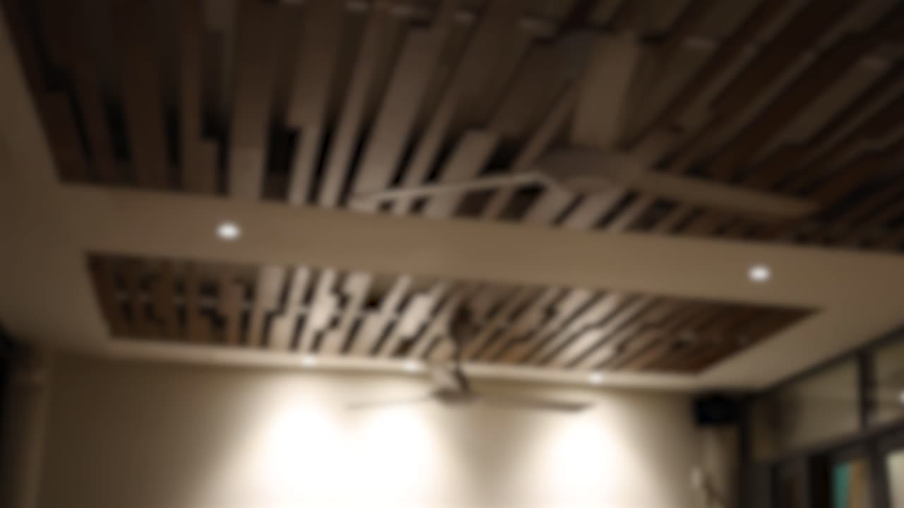 A ceiling fan rotates in a softly lit room, creating a blurred effect against a structured ceiling design