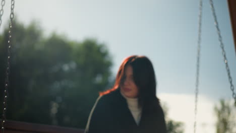 close-up of a woman adjusting her hair while swinging, with sunlight reflecting on her and lush greenery in the background, capturing a peaceful moment