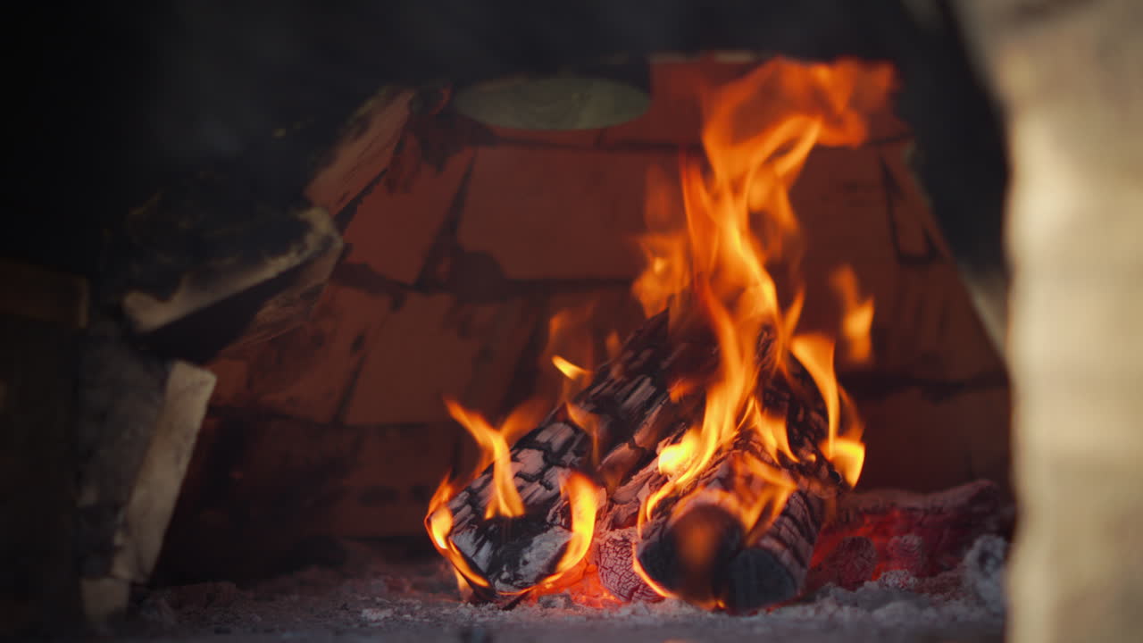 A close-up view of burning firewood inside a rustic stone oven, with bright flames and glowing embers