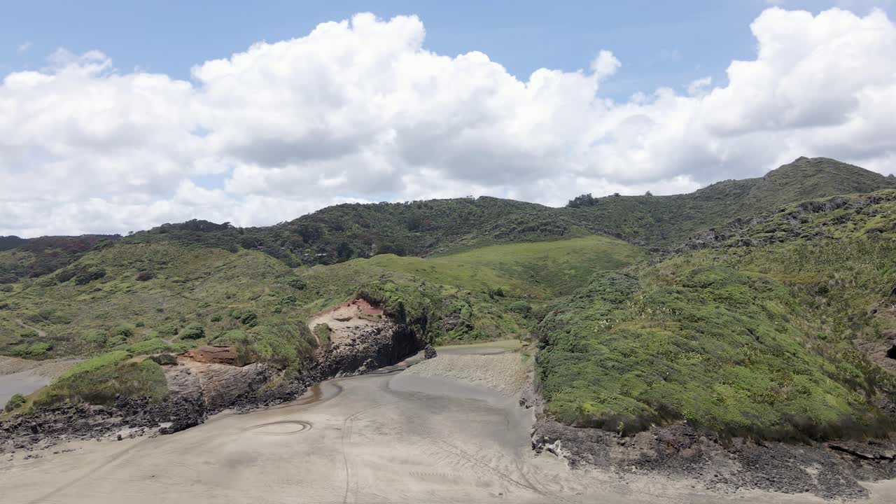 exuberantes colinas y montañas contra el cielo azul nublado en la playa de bethells, nueva zelanda - toma aérea de drones
