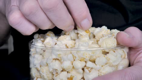 primer plano de la mano de un hombre sacando palomitas de maíz de un cubo de plástico mientras ve la televisión en casa