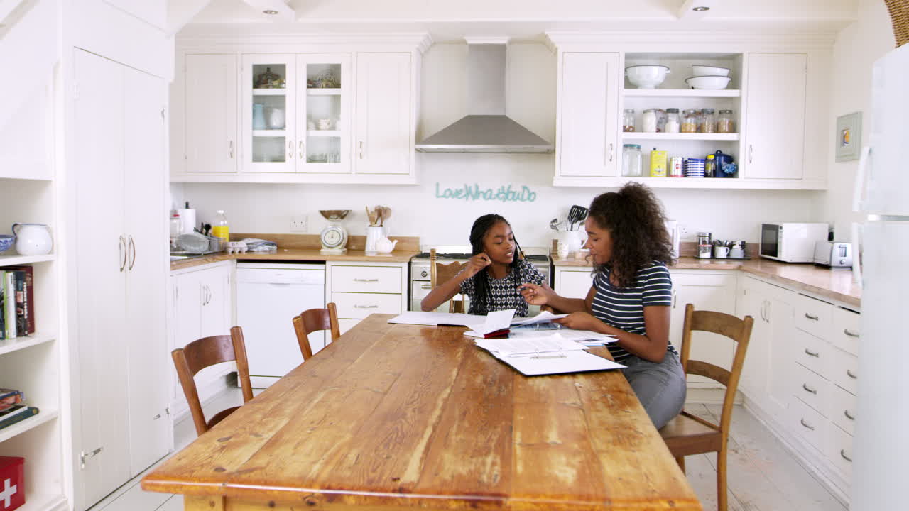 Two Sisters Sitting At Table In Kitchen Doing Homework