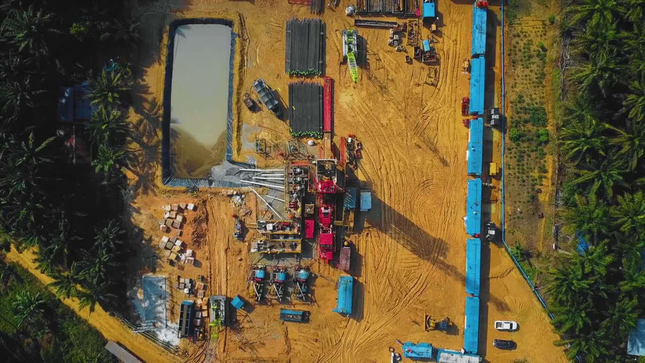 Cinematic Onshore Drilling and Workover Rig structure and Rig equipment for oil exploration and exploitation in the middle of jungle surrounded by palm oil trees during sunset time.