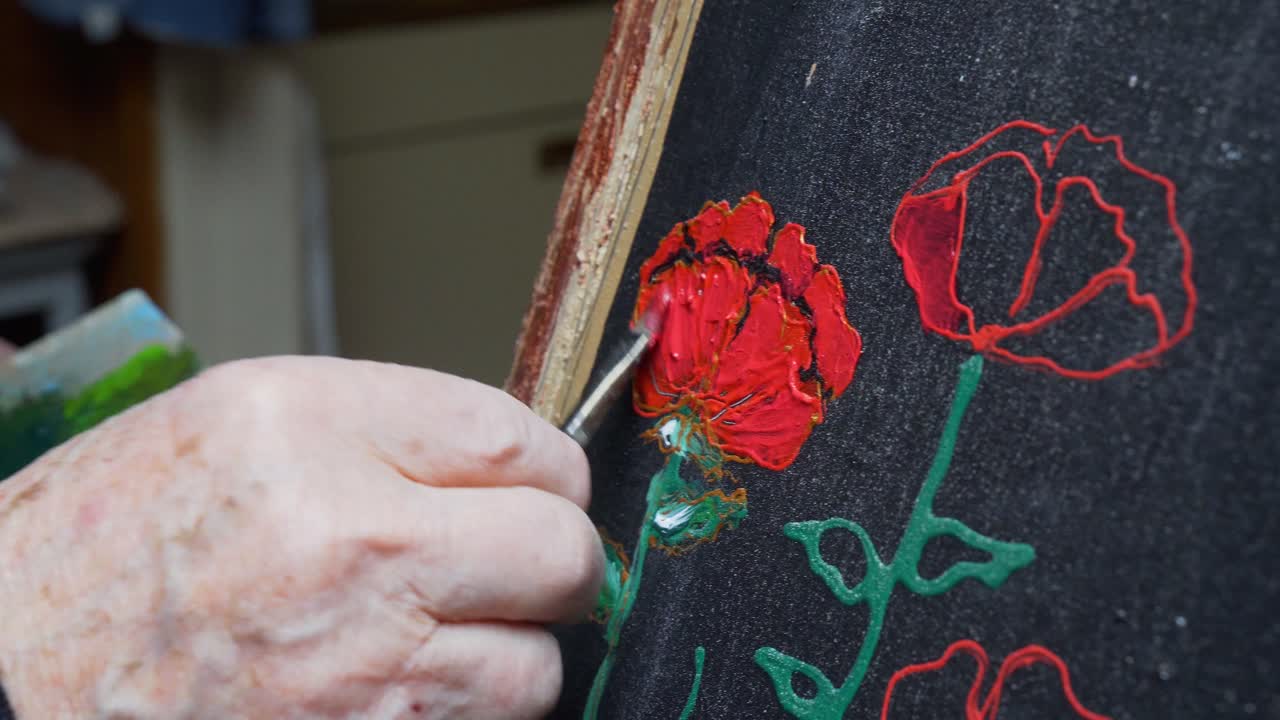 Senior male gently painting and perfecting his craft, Dabbing red paint over the black painting surface.
