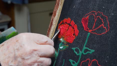 senior male gently painting and perfecting his craft, dabbing red paint over the black painting surface.