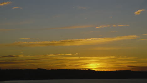 Sunrise-Timelapse-Coming-Over-Horizon-Over-Ocean-Sea-Bay-with-Small-Wind-Turbines-and-Orange-Clouds-on-Hilltop-in-Wales-UK