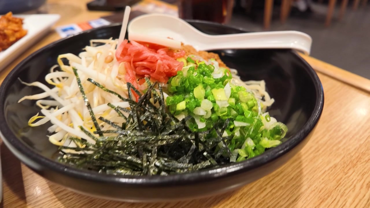 Close-up de macarrão japonês em tigela preta com coberturas coloridas em mesa de restaurante.