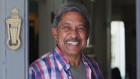 Smiling-senior-mixed-race-man-in-open-front-doorway-greeting