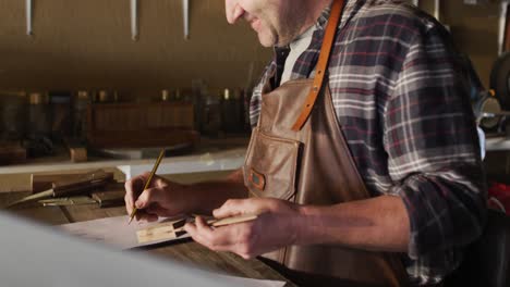 caucasian male knife maker in workshop holding tool and making notes