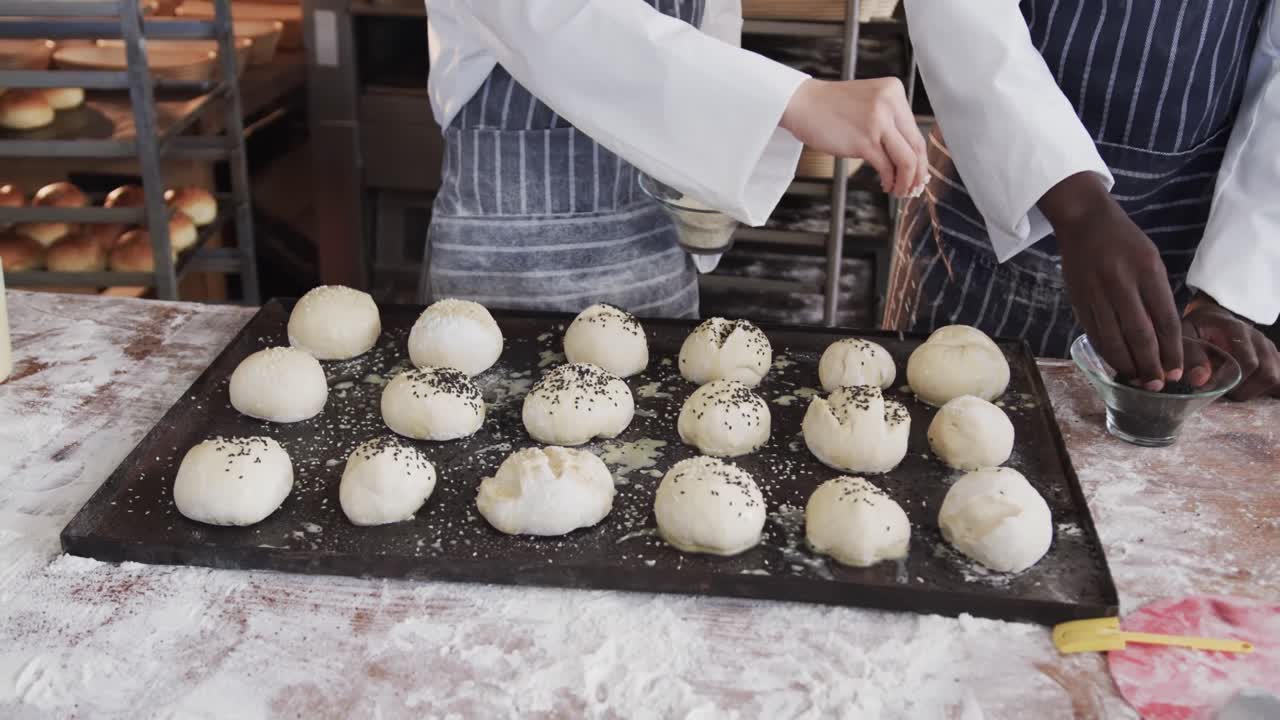 Diverse bakers working in bakery kitchen, sprinkling poppy seeds on rolls in slow motion