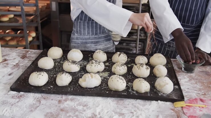 Diverse bakers working in bakery kitchen, sprinkling poppy seeds on rolls in slow motion