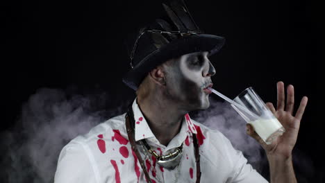 scary guy in carnival costume of halloween skeleton looking at camera, drinks milk from a glass