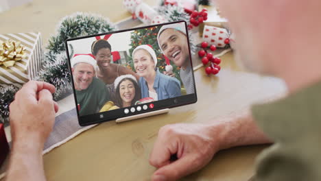 hombre caucásico con decoraciones de navidad teniendo llamada de video de tableta con diversos amigos
