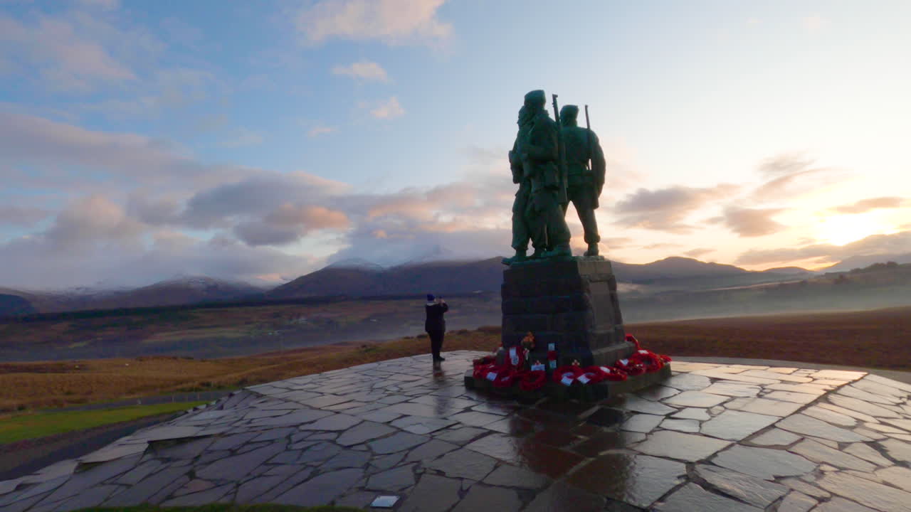 una mujer tomando fotografías del paisaje desde el memorial del comando en escocia durante la puesta de sol