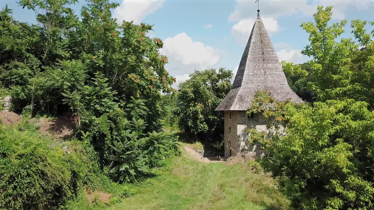 Aerial forward inside greenery towards Kushnirska Tower on a sunny day with white clouds at Kamianets Podilski,Ukraine.