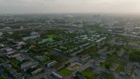backwards fly above city with buildings surrounded by trees and greenery. aerial view of neighbourhood at twilight. miami, usa