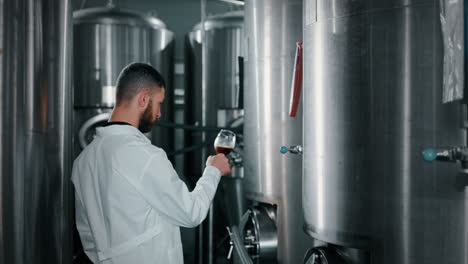 brewery worker tasting beer in production facility