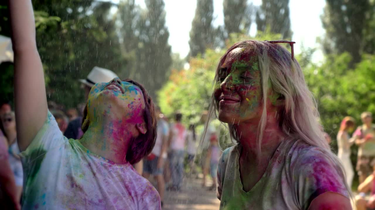 Two young happy multi-ethnic girls are enjoying rain on holi festival in daytime in summer, color concept, friendship concept