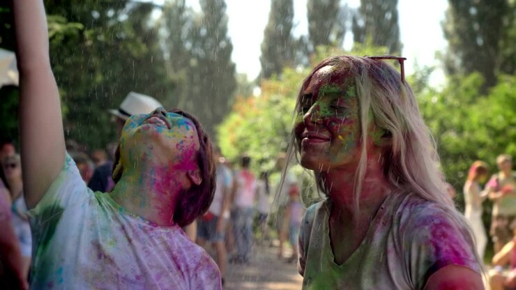 Two young happy multi-ethnic girls are enjoying rain on holi festival in daytime in summer, color concept, friendship concept