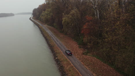 Aerial-drone-follow-of-black-luxurious-car-driving-in-a-rain---Country-riverside---Autumn-overcast