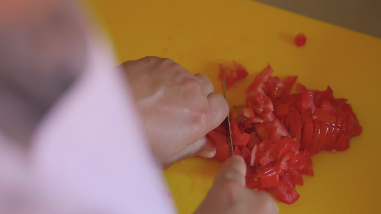 Una persona sta tagliando peperoni rossi su un tagliere giallo. Indossa una camicia bianca e sta usando un coltello per tagliare i peperoni.
