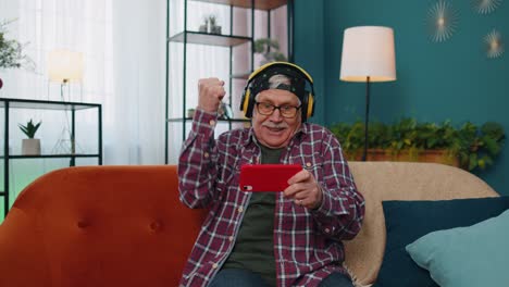 preocupado gracioso anciano anciano abuelo hombre jugando shooter juegos de video en línea en el teléfono móvil en casa