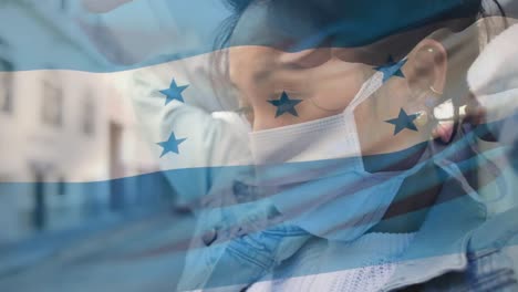 Animation-of-flag-of-honduras-waving-over-african-american-woman-wearing-face-mask-in-city-street