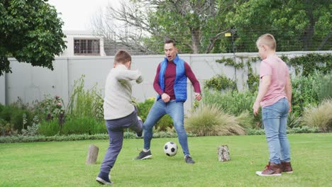 Glücklicher-Kaukasischer-Vater-Mit-Zwei-Söhnen,-Die-Im-Garten-Fußball-Spielen